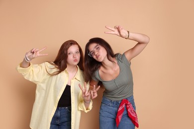 Cute teenage girls showing peace signs on beige background