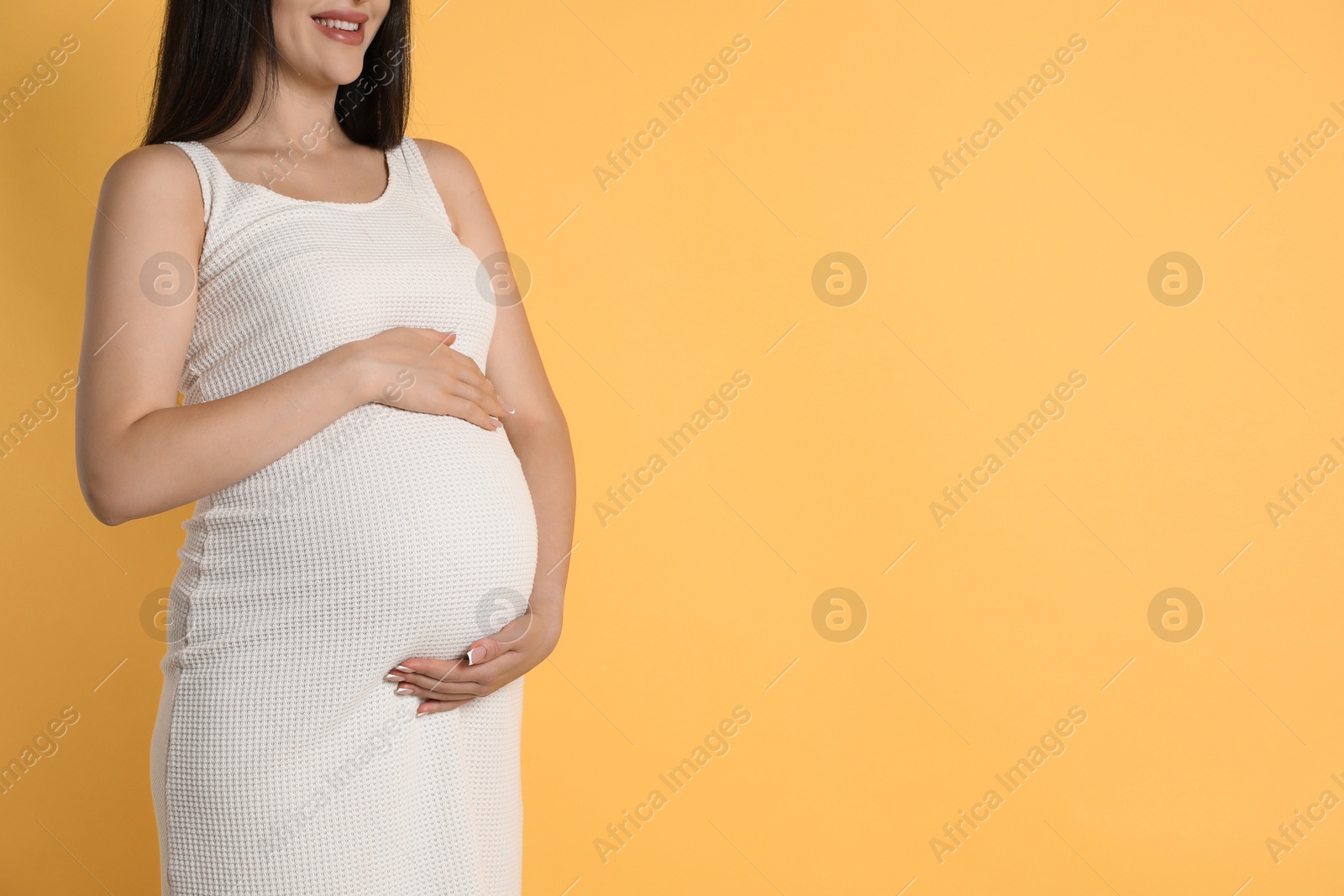 Photo of Young pregnant woman on yellow background, closeup. Space for text