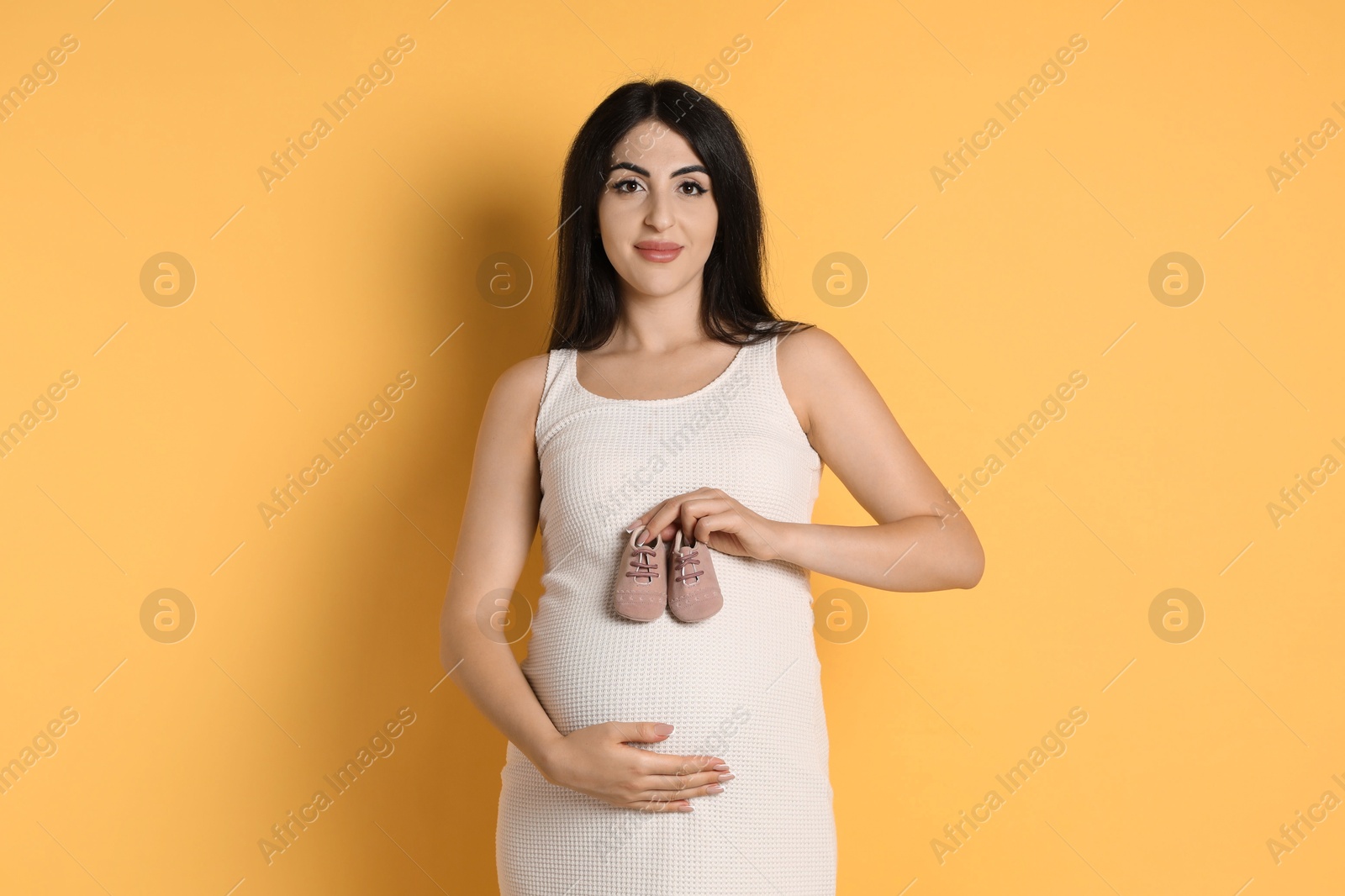 Photo of Portrait of beautiful pregnant woman with baby shoes on yellow background