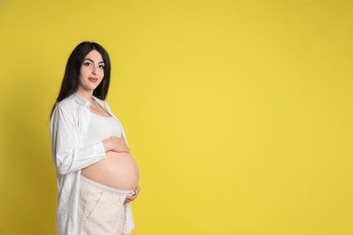 Portrait of beautiful pregnant woman on yellow background, space for text