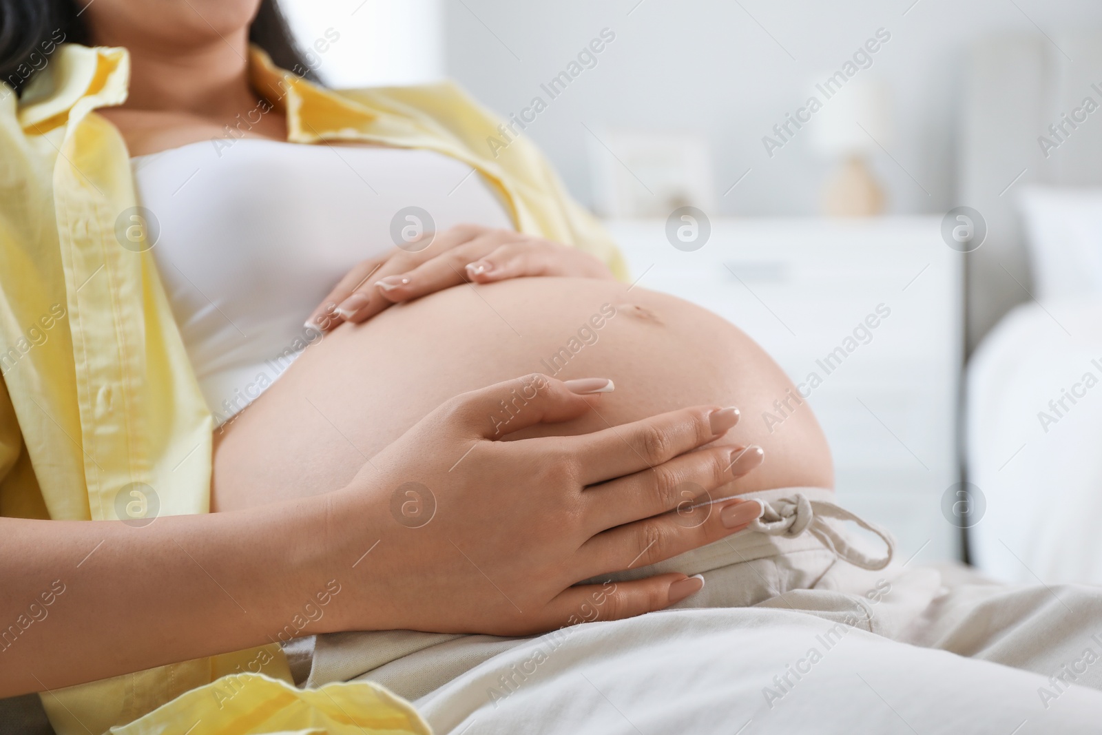 Photo of Young pregnant woman lying on bed at home, closeup