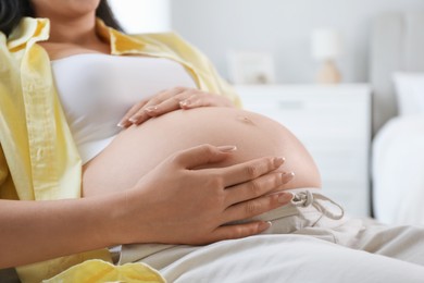 Photo of Young pregnant woman lying on bed at home, closeup