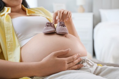 Young pregnant woman with baby shoes lying on bed at home, closeup