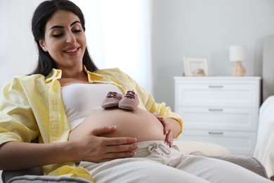 Photo of Young pregnant woman with baby shoes lying on sofa at home