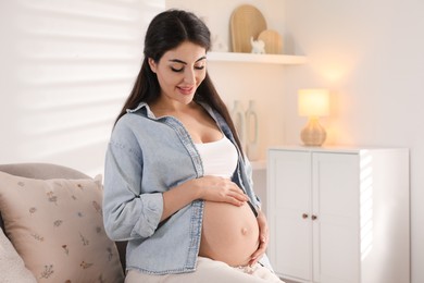 Photo of Young pregnant woman sitting on sofa at home, space for text