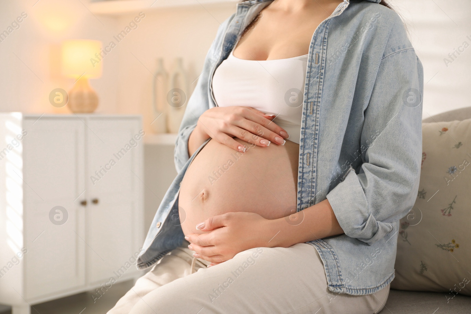 Photo of Young pregnant woman sitting on sofa at home, closeup