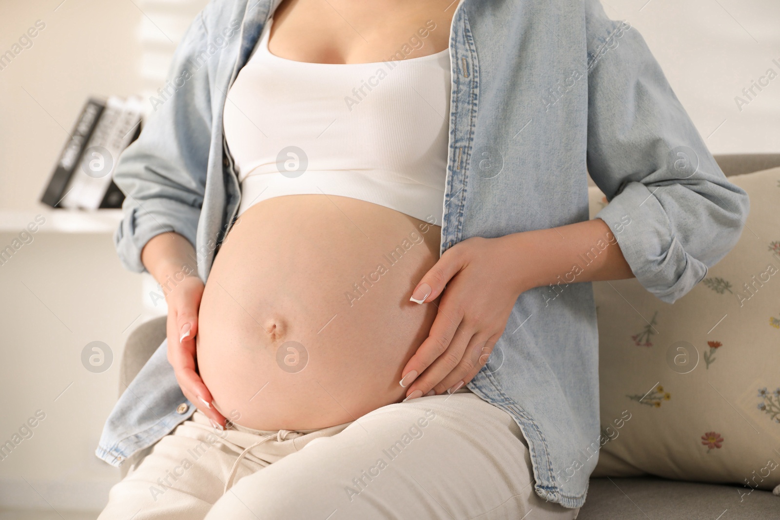 Photo of Young pregnant woman sitting on sofa at home, closeup