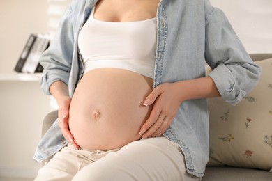 Photo of Young pregnant woman sitting on sofa at home, closeup