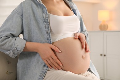 Photo of Young pregnant woman sitting on sofa at home, closeup