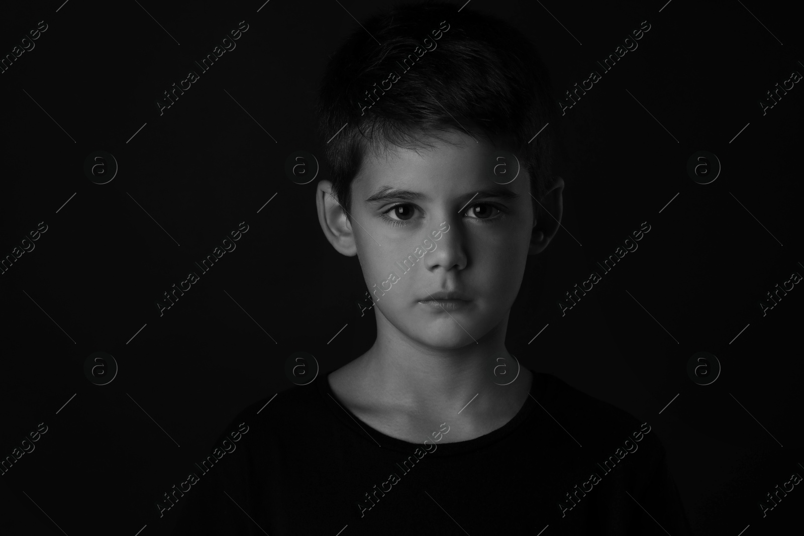 Photo of Portrait of sad little boy on dark background. Black and white effect