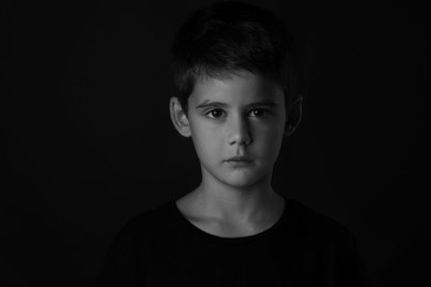 Photo of Portrait of sad little boy on dark background. Black and white effect