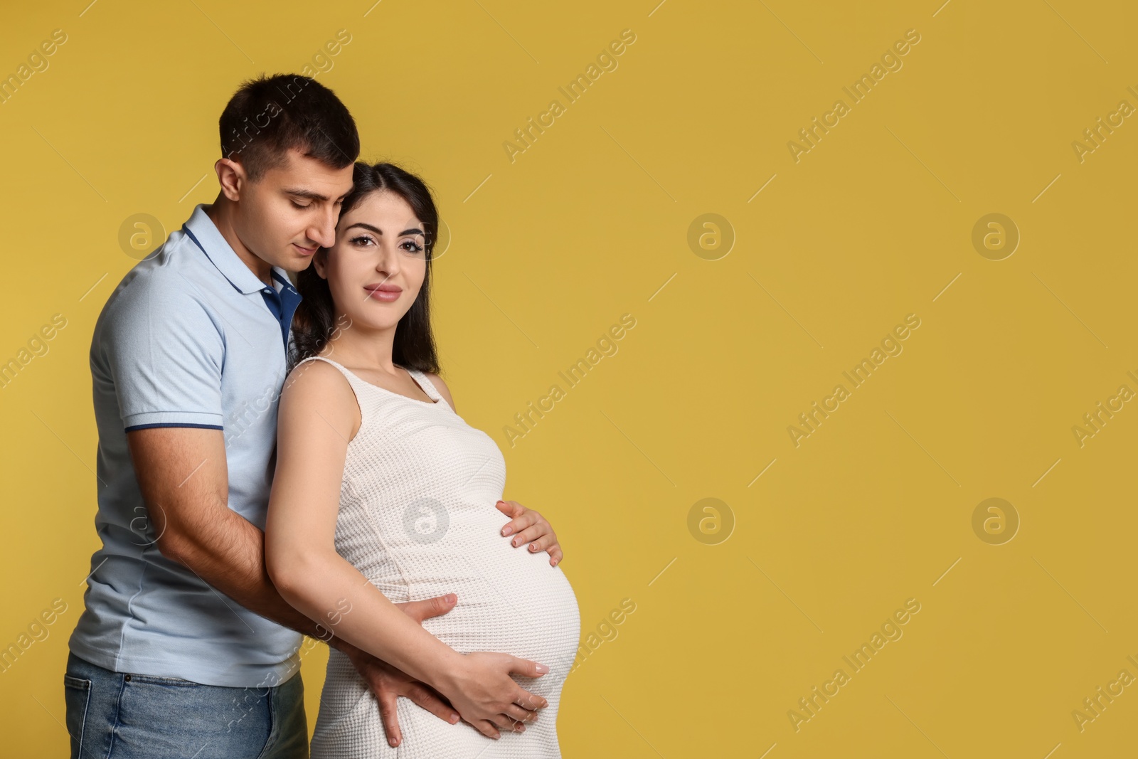 Photo of Beautiful pregnant woman with her husband on yellow background, space for text