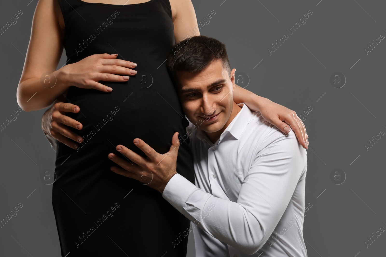 Photo of Pregnant woman with her husband on grey background, closeup