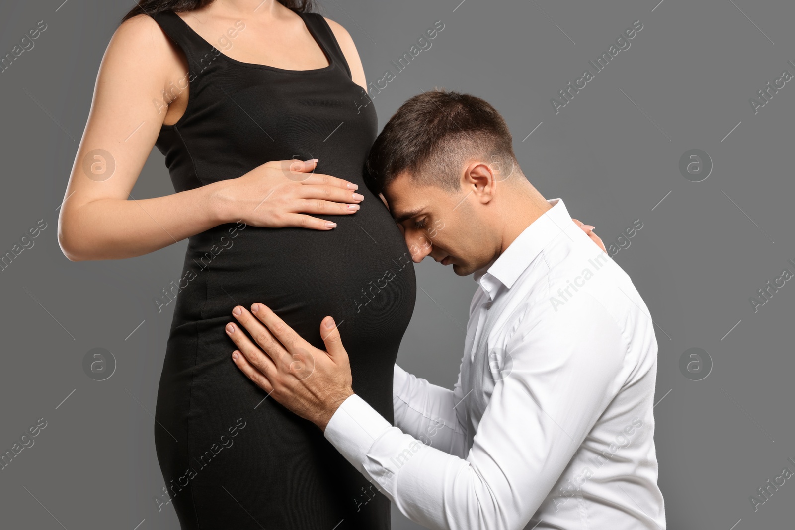 Photo of Pregnant woman with her husband on grey background, closeup