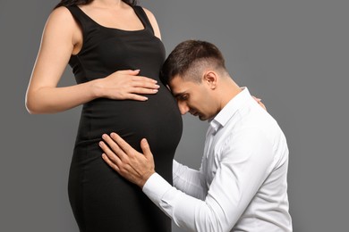 Photo of Pregnant woman with her husband on grey background, closeup