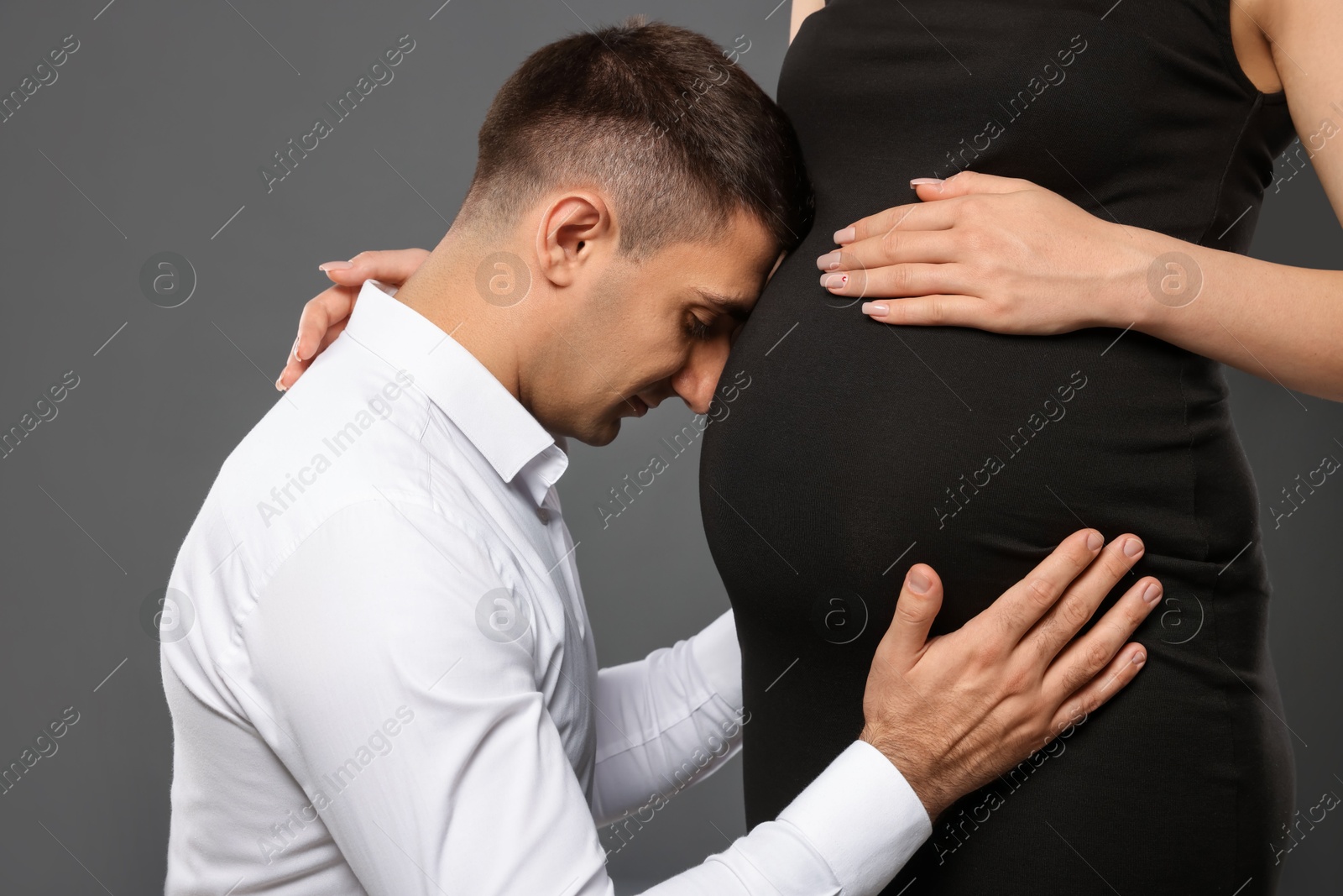 Photo of Man touching his pregnant wife's belly on grey background