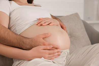 Photo of Man touching his pregnant wife's belly indoors, closeup