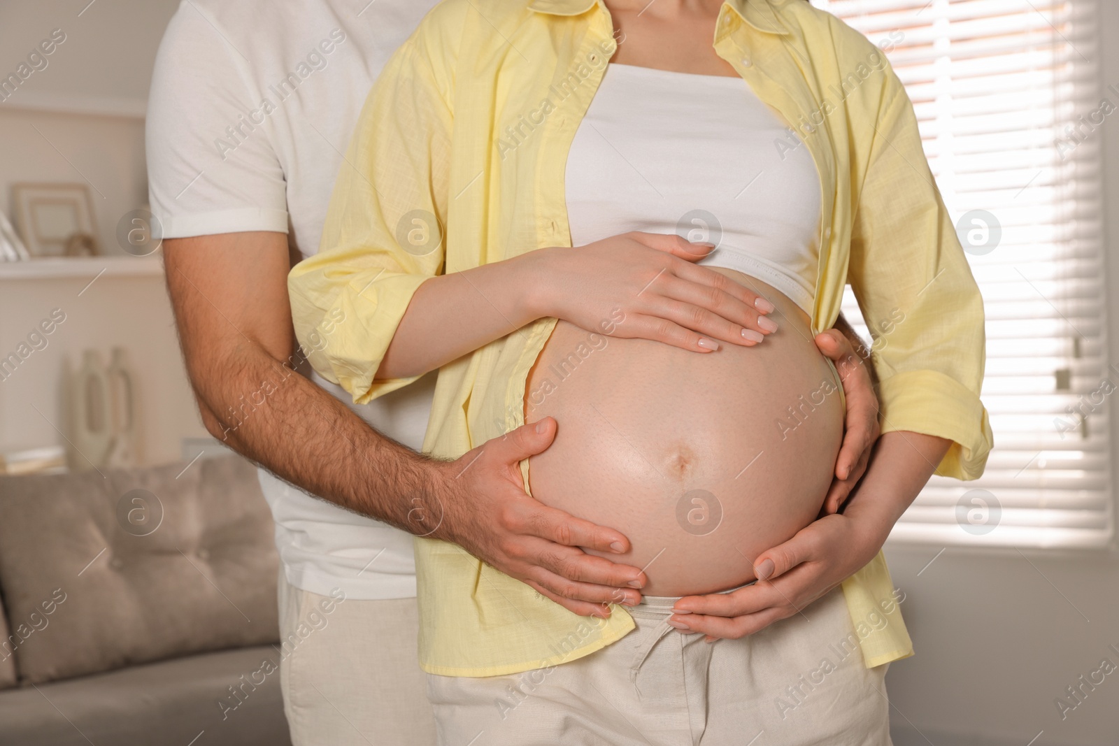 Photo of Man touching his pregnant wife's belly indoors, closeup