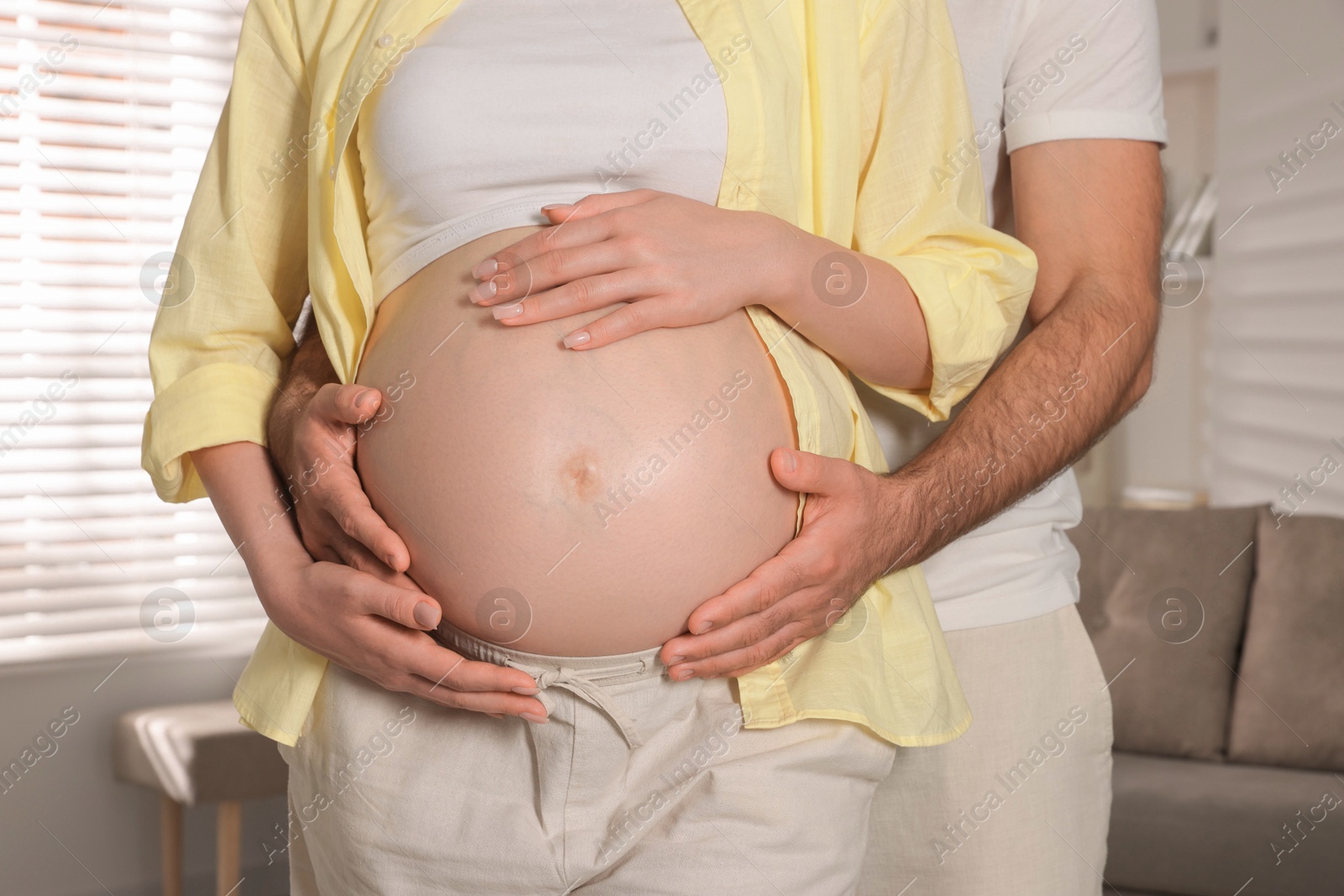 Photo of Man touching his pregnant wife's belly indoors, closeup