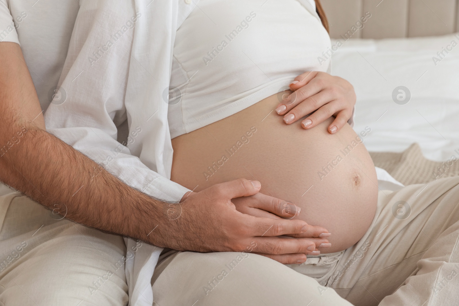 Photo of Man touching his pregnant wife's belly indoors, closeup