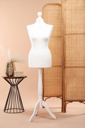 Photo of One female mannequin on stand, folding screen, coffee table with decorative plants and round box against beige background