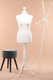 Photo of One female mannequin, rack, hanger and ottoman on beige background