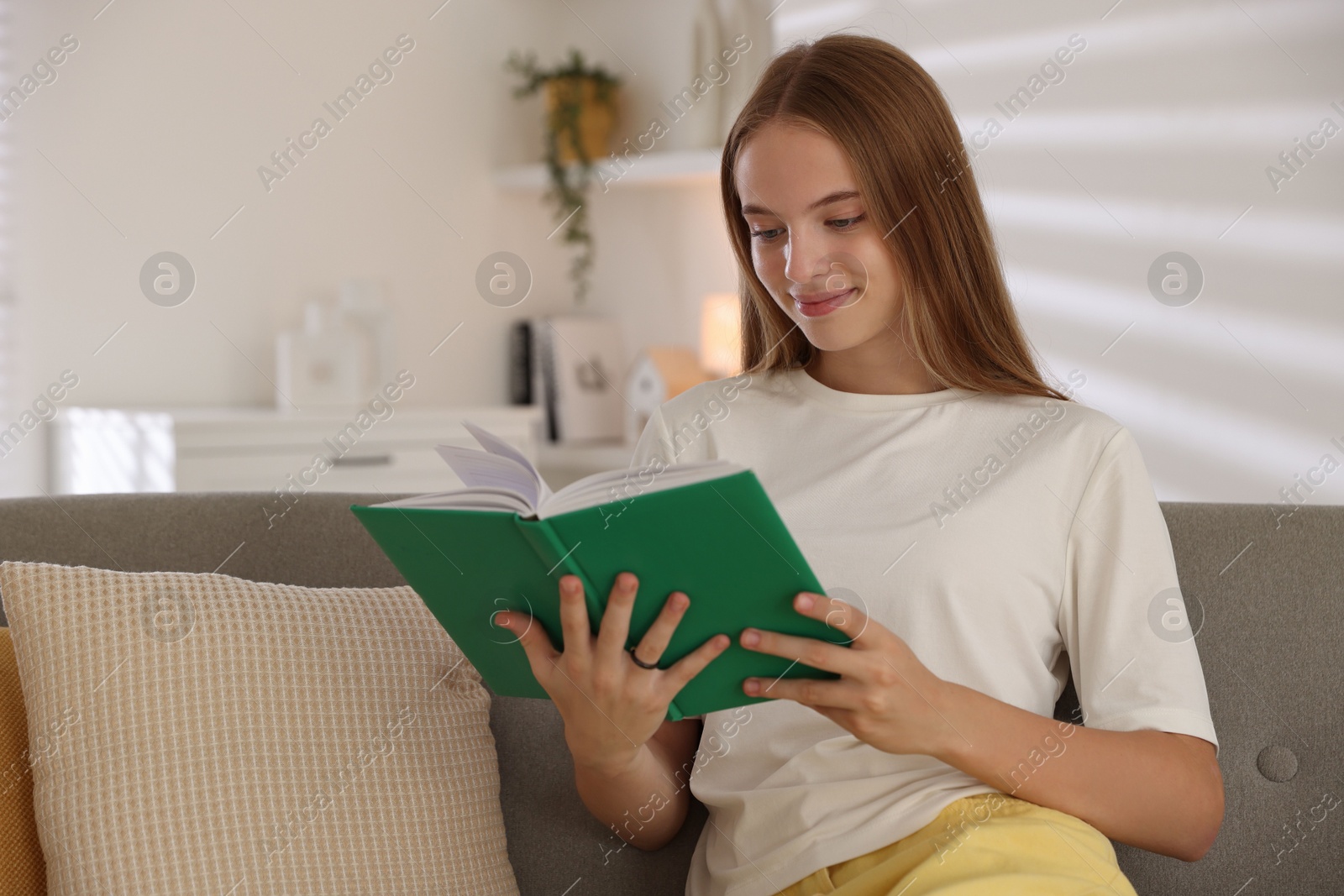 Photo of Teenage girl reading book on sofa at home