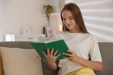 Teenage girl reading book on sofa at home