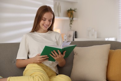 Teenage girl reading book on sofa at home