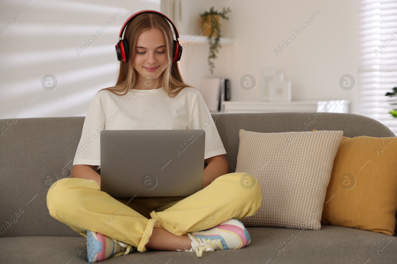 Photo of Teenage girl in headphones using laptop on sofa at home