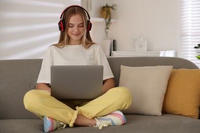 Photo of Teenage girl in headphones using laptop on sofa at home