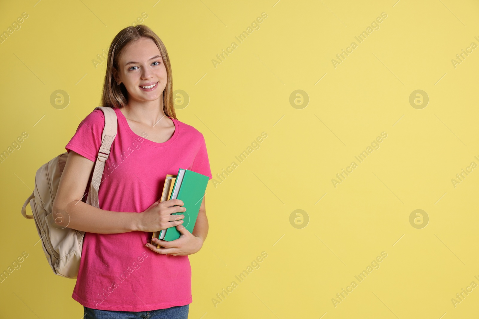 Photo of Teenage girl with books and backpack on yellow background, space for text