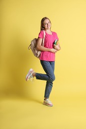 Photo of Teenage girl with books and backpack on yellow background