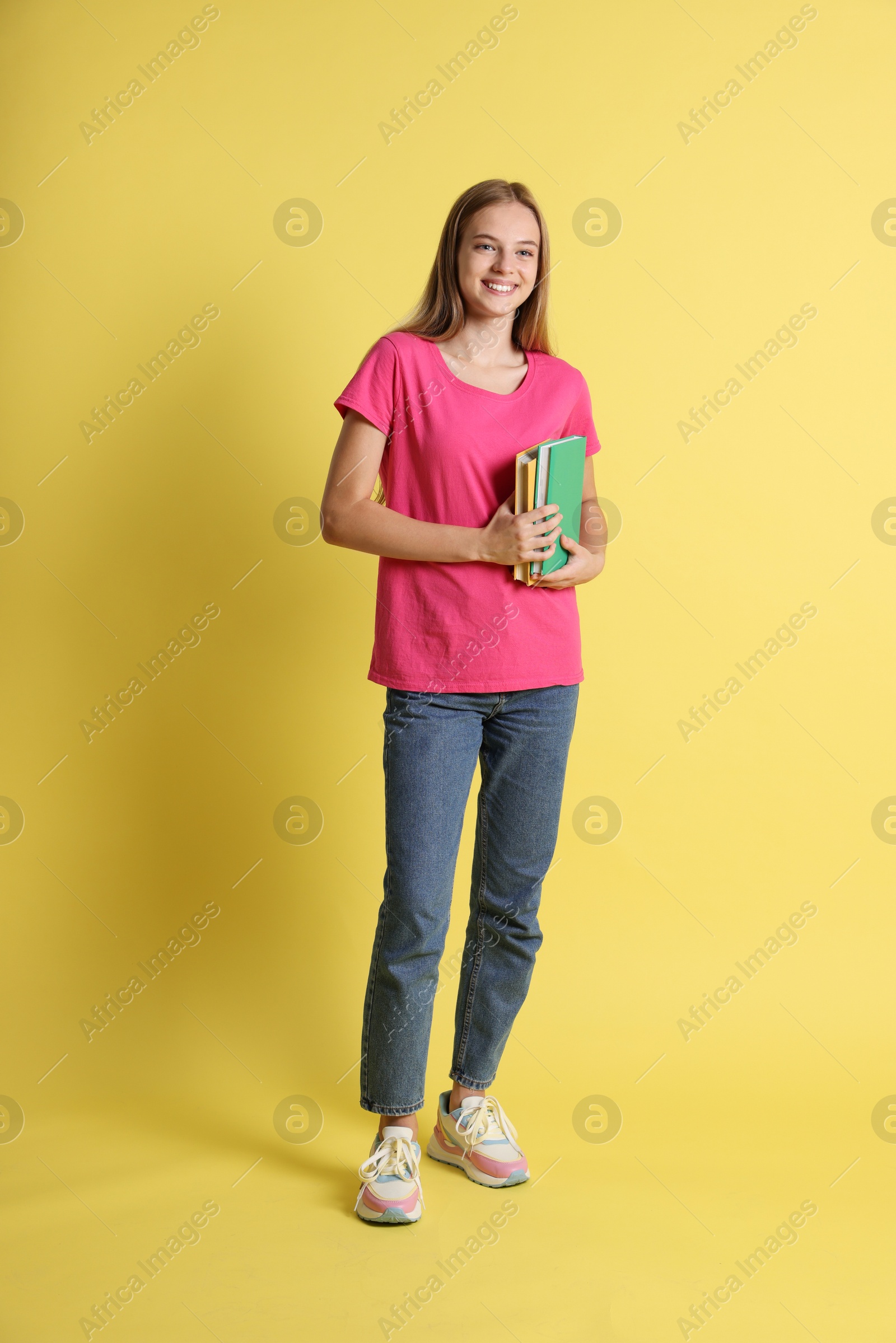 Photo of Teenage girl with books on yellow background