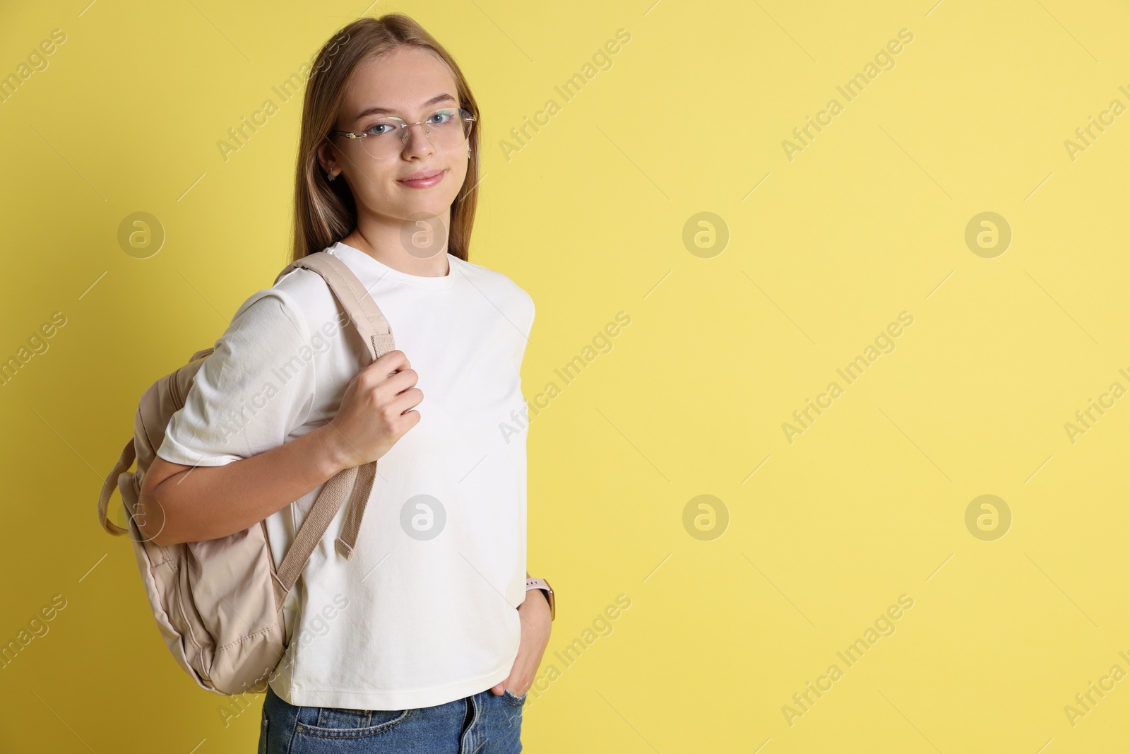 Photo of Teenage girl with backpack on yellow background, space for text