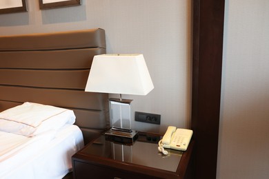 Photo of Stylish lamp and telephone with handset on bedside table in hotel room