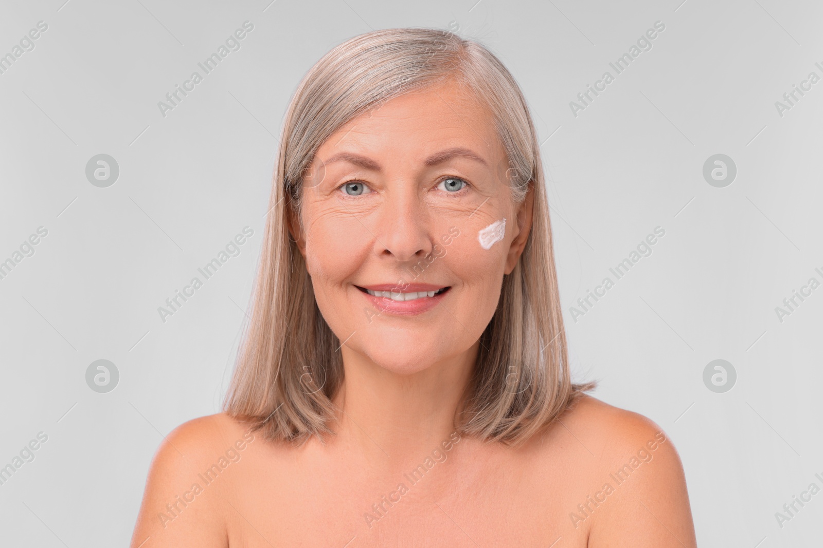 Photo of Senior woman with face cream on white background