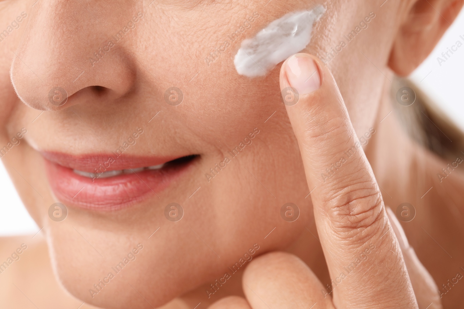 Photo of Senior woman applying face cream on white background, closeup