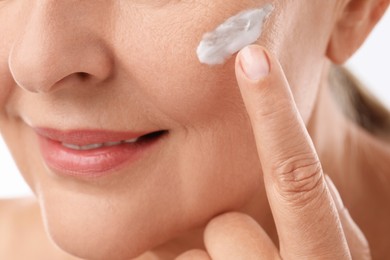 Photo of Senior woman applying face cream on white background, closeup