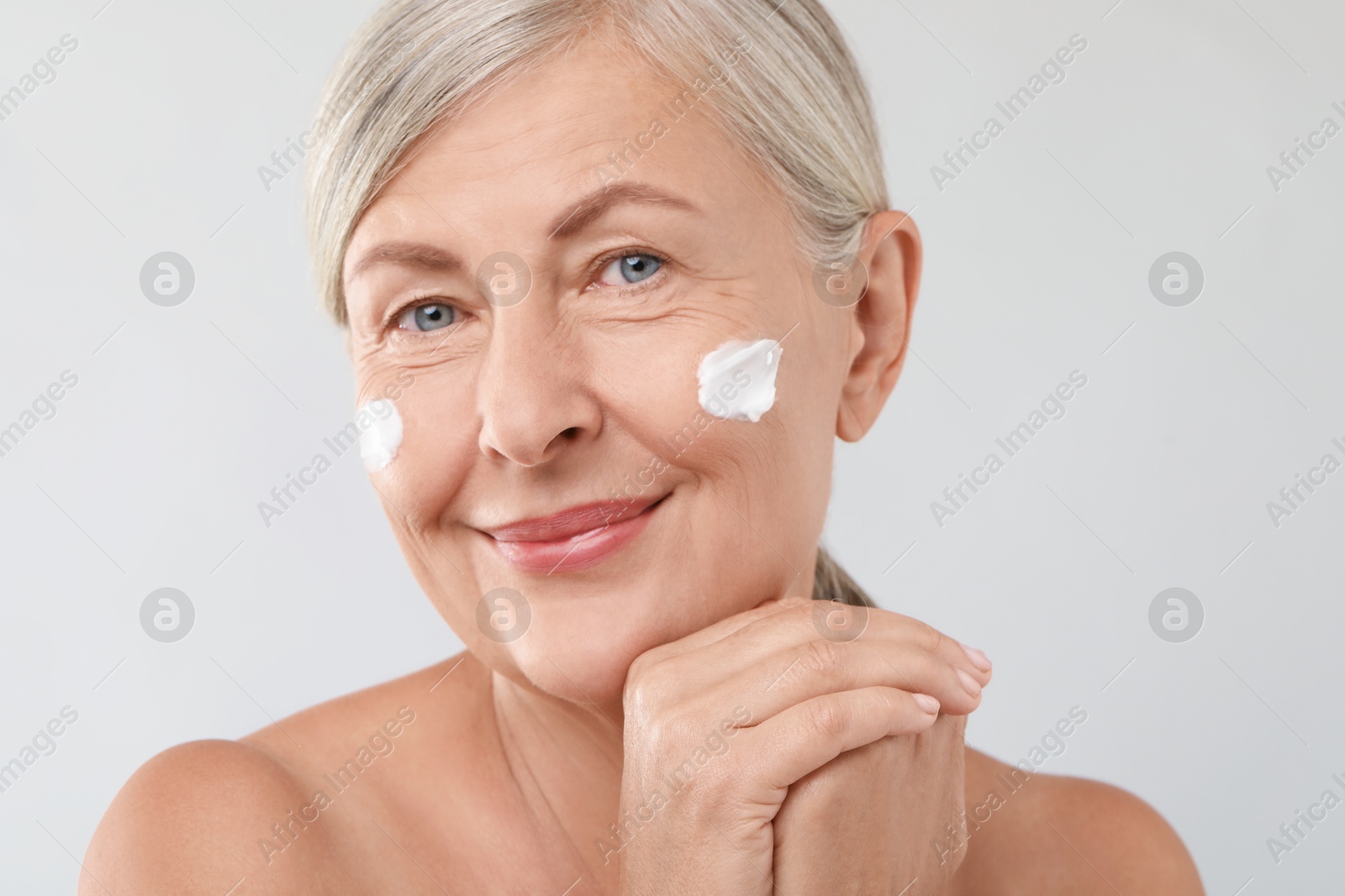 Photo of Senior woman with face cream on light background, closeup