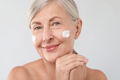 Senior woman with face cream on light background, closeup