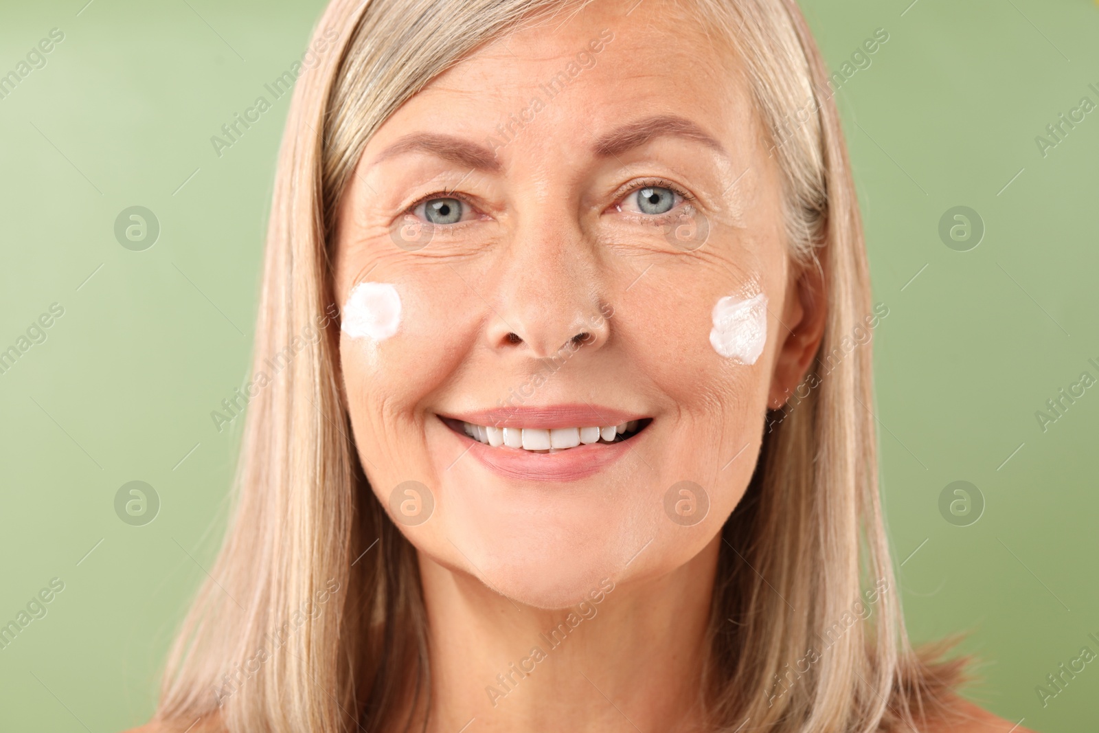 Photo of Senior woman with face cream on green background, closeup