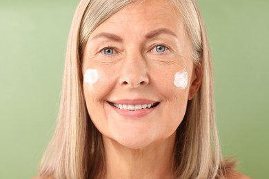 Photo of Senior woman with face cream on green background, closeup