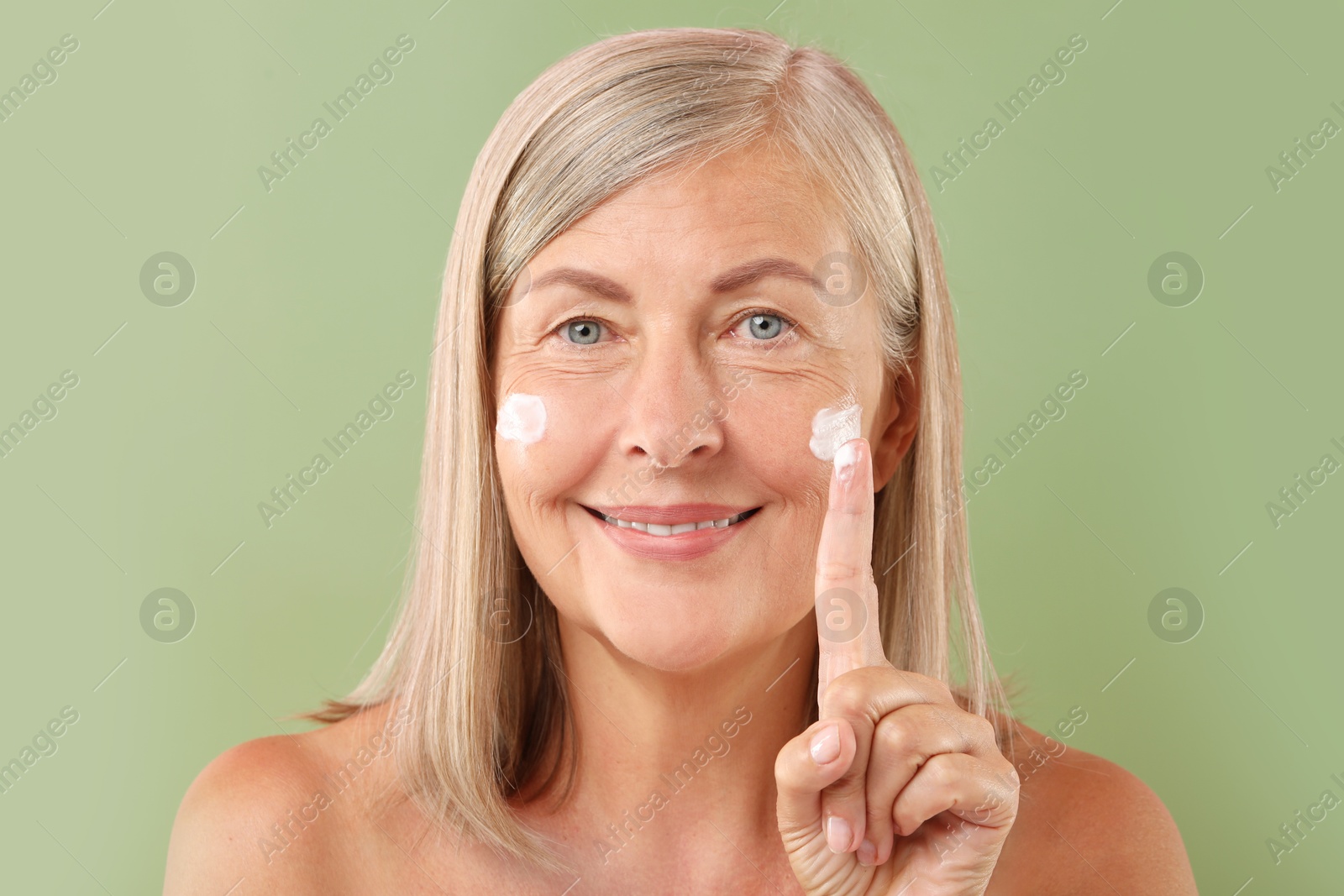 Photo of Senior woman applying face cream on green background