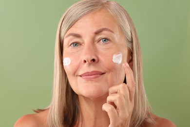 Senior woman applying face cream on green background