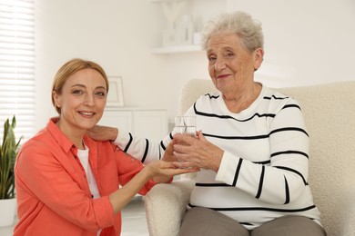 Photo of Caregiver giving glass of water to senior woman at home