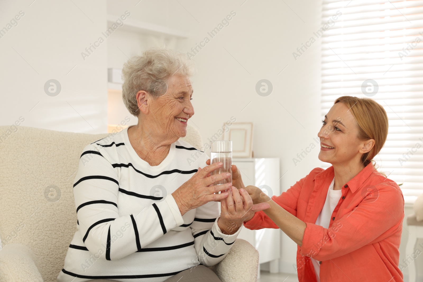 Photo of Caregiver giving glass of water to senior woman at home