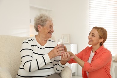 Caregiver giving glass of water to senior woman at home