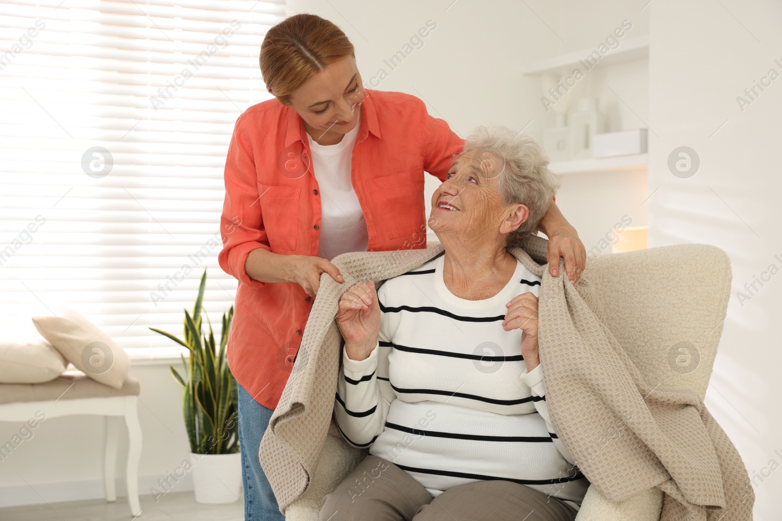 Photo of Caregiver covering senior woman with blanket at home