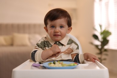 Cute little baby eating healthy food in high chair at home